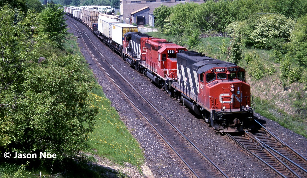 CN intermodal train 144 with GP40-2(W) 9647, SD40-2 5391 and GP40-2L(W) 9458 are passing the Georgetown, Ontario station as they head eastbound on the Halton Subdivision. CN 5391 is ex-CP 5782, which was part of a group of units originally owned by Ontario Hydro.