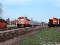 CP Rail train #11, "The Canadian", highballs through downtown Woodbridge during the final months of CP operation (before CP handed most of its passenger operations over to VIA in September 1978). Former AM Road "Silver Streak" Hollywood star CP FP7 4067 leads a short Toronto-Sudbury consist solo, only 5 stainless steel cars long (baggage-dorm, coach, Skyline dome, diner & sleeper) and run without a Park car in its last CP years. The train has just passed Kipling Avenue (8th Line) and is passing the sectionman's shack by the private crossing to Woodbridge Foam.<br><br>In the foreground is the south end of the Woodbridge siding/passing track. CP 8107, one of the local Toronto-assigned SW1200RS units, works a wayfreight on the former Toronto, Grey & Bruce (TG&B) spur, that was once the mainline through town (until CP realigned the line in 1907-08, shifting the mainline track to the east through downtown Woodbridge on a new alignment). The north section of the old TG&B alignment here remained as a short spur serving a few local Woodbridge industries, including Woodbridge Foam (ex-Robson's Cotton Mill), Woodbridge Lumber, a team track and ramp, fuel dealer, grain elevator, and a farm supply co-op operating out of the original TG&B Woodbridge Station, that still existed (!) into the mid-1970's until it was demolished for a new fire station and the Woodbridge Avenue road extension west of Kipling.<br><br>By this time the CPR's own Woodbridge Station, that once stood near the end of the train to the right, had been demolished a number of years prior (officially closed May 1968, no more passenger service for Woodbridge), so the next station stop for #11 after departing Toronto Union Station would be Bolton. Kleinburg Station in the hamlet of Nashville, the next stop north, had also been closed by this time (but was saved from demolition and moved into Kleinburg proper for preservation).<br><br>Many changes have occurred here since: the TG&B Spur is no more (the last remains behind Nino D'Aversa bakery removed around 2025 for a new townhouse complex), the lumberyard is now townhouses, and The Canadian left CP's rails not long into the VIA era. Woodbridge Foam still exists here, as do many of the old heritage houses in the background along Kipling (that one house in the background, located right next to the grade crossing, is now home to Condello Trucking/Condor Float Service).<br><br><i>Barry Schroeder photo, Dan Dell'Unto slide collection.</i> <br><br> More of The Canadian in Woodbridge:<br> CP #11 crossing the Highway 7 bridge: <a href=http://www.railpictures.ca/?attachment_id=42540><b>http://www.railpictures.ca/?attachment_id=42540</b></a><br> CP #12 past the Humber River bridge: <a href=http://www.railpictures.ca/?attachment_id=25984><b>http://www.railpictures.ca/?attachment_id=25984</b></a><br> CP #11 at Langstaff Ave underpass: <a href=http://www.railpictures.ca/?attachment_id=47972><b>http://www.railpictures.ca/?attachment_id=47972</b></a><br> CP #12 heading south past Highway 7: <a href=http://www.railpictures.ca/?attachment_id=36502><b>http://www.railpictures.ca/?attachment_id=36502</b></a><br> CP #11 at Highway 27 underpass: <a href=http://www.railpictures.ca/?attachment_id=1644><b>http://www.railpictures.ca/?attachment_id=1644</b></a>