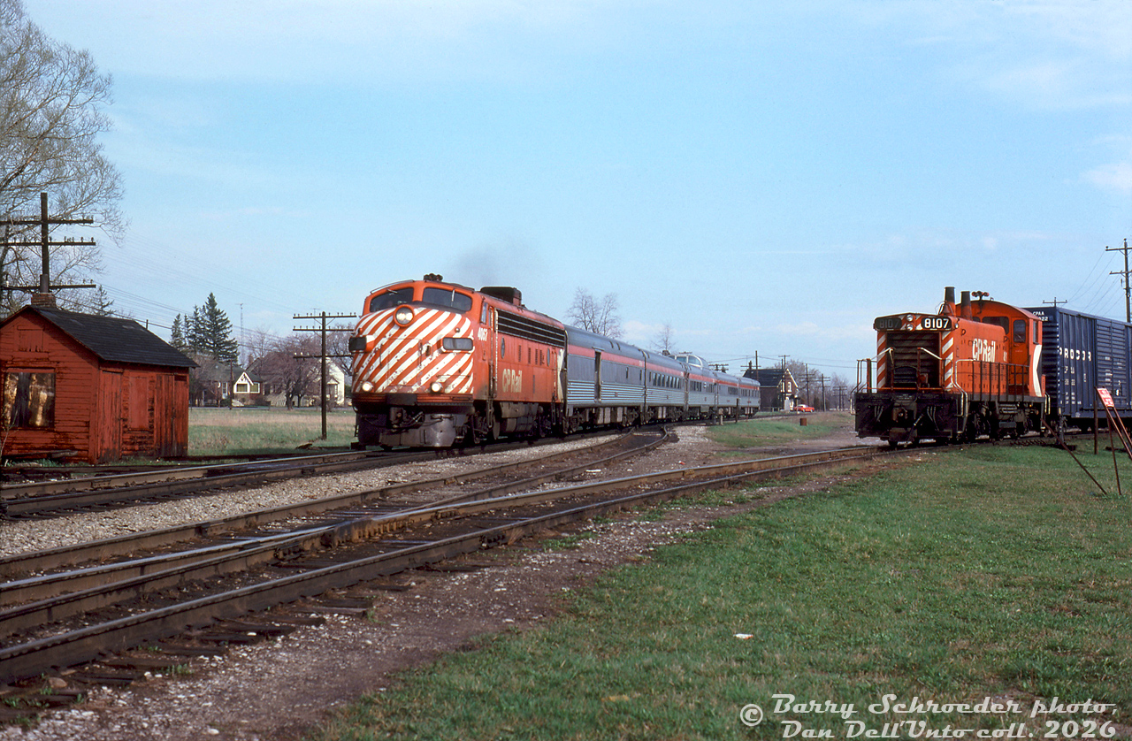 CP Rail train #11, "The Canadian", heads through downtown Woodbridge during the final months of CP operation (before CP handed most of its passenger operations over to VIA in September 1978). CP FP7 4067 leads a short Toronto-Sudbury consist solo, only 5 stainless steel cars long (baggage-dorm, coach, Skyline dome, diner & sleeper) and run without a Park car in its last CP years. The train has just passed Kipling Avenue (8th Line) and is passing the sectionman's shack by the private crossing to Woodbridge Foam.

In the foreground is the south end of the Woodbridge siding/passing track. CP 8107, one of the local Toronto-assigned SW1200RS units, works a local wayfreight on the former Toronto, Grey & Bruce (TG&B) spur, that was once the mainline through town (until CP realigned the line around 1907-ish, shifting the mainline track to the east through downtown Woodbridge on a new alignment). The north section of the old TG&B alignment here remained as a short spur serving a few local Woodbridge industries, including Woodbridge Foam (ex-Robson's Cotton Mill), Woodbridge Lumber, a team track and ramp, fuel dealer, grain elevator, and a farm supply co-op operating out of the original TG&B Woodbridge Station, that still existed (!) into the mid-1970's until it was demolished for a new fire station and the Woodbridge Avenue road extension west of Kipling.

By this time the CPR's own Woodbridge Station, that once stood near the end of the train to the right, had been demolished a number of years prior (officially closed May 1968), so the next station stop for #11 after departing Toronto Union Station would be Bolton. Kleinburg Station in the hamlet of Nashville, the next stop north, had also been closed by this time (but was saved from demolition and moved into Kleinburg proper for preservation).

Many changes have occurred here since: the TG&B Spur is no more (the last remains behind Nino D'Aversa bakery removed around 2025 for a new townhouse complex), the lumberyard is now townhouses, and The Canadian left CP's rails not long into the VIA era. Woodbridge Foam still exists here, as do many of the old heritage houses in the background along Kipling (that one house in the background, located right next to the grade crossing, is now home to Condello Trucking/Condor Float Service).

Barry Schroeder photo, Dan Dell'Unto slide collection.