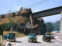 High over traffic on the Paterson-Trail Highway below, Canadian Pacific H24-66 "Train Master" 8905 passes above on the Rossland Sub at Warfield, BC, climbing the grade to the nearby smelter at Trail. The photographer's green VW bus sits pulled over to the side, with a companion along for the ride watching the Train Master come into view and cross over the bridge.<br><br>Once part of a group of 21 units, by the early 70's the trio of CP 8900, 8904 and 8905 were based out of CP's Nelson BC shop for maintenance, and assigned to Trail for switching the Cominco smelter. This assignment also involved bringing trains up the Rossland Sub's steep Warfield Hill, a heavy drag-type assignment that once involved CP's only Lima Shay steam locomotives (units 1901-1903) that brought cars up the steep grades (4.1%!) and switchbacks. "Shorty vans" were used because of a switchback enroute, in order to allow the maximum amount of cars (two vans, 437110 and <a href=http://www.railpictures.ca/?attachment_id=36643><b>437111</b></a>, were shortened in 1944, and continued to see use into the 1970's).<br><br>Over time the trio of Trail units became the last three Train Masters on the system (as Montreal's units were retired in 1972). They were then sent to Alyth Yard for <a href=https://www.railpictures.ca/?attachment_id=32660><b>hump service</b></a> in September 1973, and stored in December 1975 (replaced by GP7's due to complaints about their exhaust fumes getting sucked into the yard office by the hump). After being <a href=http://www.railpictures.ca/?attachment_id=40661><b>"Tied Up Unserviceable" in 1976</b></a>, the order was given from the higher ups to scrap them. 8900 and 8904 were cut up at Ogden Shops in August 1976, while 8905 was set aside as part of CP's historic diesel collection earmarked for future preservation (8905 now resides at Exporail/CRM in Delson, QC, the last Train Master in existence).<br><br>A story from the late Bruce Chapman was before they were reassigned to Alyth, the motive power department tried to find another home for them to work out of. They were told in no uncertain terms by the brass out east that there was absolutely no place for them to be used on the Eastern Region (that had retired the last of theirs from transfer service: Montreal-based units 8901, 8909 and 8917).<br><br><i>Eric W. Johnson photo, Dan Dell'Unto collection slide</i>.