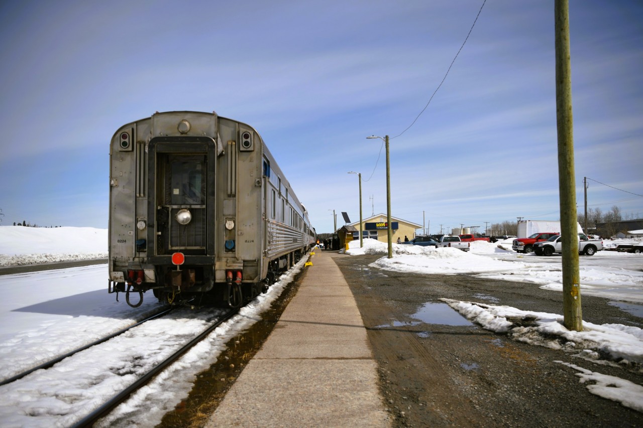 A paddle on the rear  
VIA 8224 Chateau Roberval carries the markers (or in today's display, the paddle) on the rear of VIA 692. 
Backed into the station at Thompson, MB for its scheduled stop, passengers mill about the station area, baggage gets handled by local VIA personnel, and the head end crew swaps out. 
There is still a lot of snow on the ground for May 1st. There are concerns for the amount of water that will be present along the right-of-way when the melt comes.