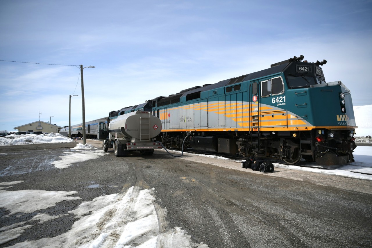 Takin' on some juice  
VIA 692 has backed into the station at Thompson, MB for its regular scheduled stop. 
Passengers have a few hours to mill about the station and surrounding area, go into town for a walk and maybe a little Walmart shopping, or wait in the parking lot for a driver to show up with pre-ordered restaurant food from one of the many local beaneries. I chose to get a large 'all meat' pizza from Santa Maria Pizza which was delivered quickly and was still hot as it was enjoyed in the dining area of the Skyline Car. 
The head-end crew is in the process of changing out for a fresh team of engineers as a local diesel fuel supplier has the nozzle in place and is topping up the tanks on VIA 6421 and VIA 6455. 
All of the VIA personnel were very accommodating in my efforts to get all the head end shots I wanted at every stop made along the way from Winnipeg to Churchill and return. :-)