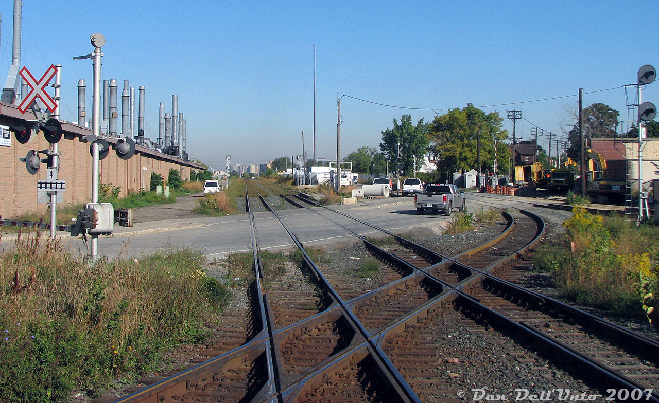 Another set of the diamonds, but not "the" diamonds: the rear truck of GO cab car 237 clatters over one of the diamonds for the CP connecting track at West Toronto, that connected the MacTier Sub to the North Toronto Sub. Our train, GO #252, has just cleared Old Weston Road crossing on the double track CN Weston Sub and is still crossing over the actual diamonds with the double track CP North Toronto Sub (out of view to the south). CP's MacTier Sub mainline can be seen on the far right. In the distance, both CN tracks become one at CN Keele.

Looking north, one can make out the old platforms for the former CN West Toronto Station, finally demolished only 8 years ago. The fenced-in area where the station and express building once were was home to a compound lot used for storing snow removal equipment over the summer (the equipment was owned by Westridge Agriculture, which had one of the city snowplowing contracts, and they had rows and rows of old Champion and Wabco graders parked here). The building on the left was National Rubber Industries' Cawthra Ave plant. The Andrew Merrilees yard was just out of view on the right. Judging by the machinery and pipes, there was some sewer or water main construction going on. Today, the old station grounds are gone, the connecting track is still there, but it now goes over both CN mainlines that have been grade separated into a giant trench below.