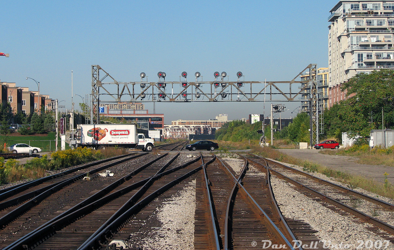 No, the cars aren't blowing the crossing: we're riding in the cab of GO cab car 237, trailing southbound on Bramalea-Toronto train #252 on the Georgetown line. The cab car is bucking through the crossovers at Strachan Avenue, just after clearing the grade crossing as traffic going through Liberty Village resumes and the train enters the Union Station Rail Corridor.

All that remained of Strachan Avenue in the mid-late 2000's was a busy grade crossing and a massive signal bridge. The old CP Parkdale Yard (once on the left) had long been removed and replaced with housing, ditto for the old Massey Harris/Ferguson manufacturing facilities on the north side (to the right). Two old CP yard spotlight towers remained (one here at Strachan out of view to the left, the other visible in the distance near King St. underpass). Most of the manufacturing buildings here had been either torn down and redeveloped, or repurposed into lofts and condos (I recall that black building in the background was another M-F factory along King St. that was later demolished). The double-track mainlines for the CP Galt Sub (left) and CN Weston Sub (right) remain. All of this was replaced with a large trench a number of years later.