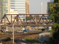 Not the conventional Bathurst Street bridge shot: this one is of the bridge itself, looking east from Strachan Avenue in nearby Liberty Village.<br><br>VIA P42DC 907 backs its 4-car LRC consist from the TMC in Mimico to Union Station in downtown Toronto, ducking underneath Bathurst Street bridge after having just entered the Union Station Rail Corridor at the signalbridge sign marker to the left. GO trains are hiding in the wings: a few consists are lined up on the right, slowly making their way to Union Station to enter PM rush-hour service. At least one lingers in Bathurst North Yard beyond the bridge to the left, almost all cleared out of consists.<br><br>Once VIA #87 arrives at Union and finishes boarding, it will make its timely departure from Toronto at 5:40pm (5 minutes ahead of Georgetown-line GO train #211 running behind it), bound for such exotic places as Brampton, Guelph, London, and ultimately Sarnia. Unfortunately when we went to shoot it at Strachan Avenue crossing on the Weston Sub, the shadows had gotten much too long for any good light to be had.