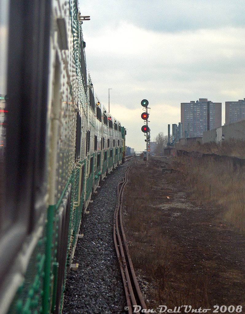 We're riding GO train #260 today (Bramalea-Union), looking at the front of our train as GO Transit F59PH 521 in the lead is about to knock down the light at CN Keele on the approach to West Toronto diamond. The double towers of the Crossways Mall are visible in the distance, as is the Wallace Avenue pedestrian footbridge near our next stop at Bloor GO Station. This consist was run as an L8 at the time (locomotive + 8 bilevels, easy to count from outside the train), and one can see the side indicator light illuminated for the 5A accessible car (the red on the other car is a reflection of the signal). The other thing that sticks out is the sheer amount of rivets on the older bilevels, pre-dating the switch to welded construction in the 90's.To appease any concerned Metrolinx staff reading this, this photo was not taken while hanging off the side of a bilevel outside of the train at speed (don't hang off the sides of moving GO trains, kids), nor was it taken poking out an open bilevel window: rather, it was the ol' "trick mirror shot", shot looking into the side mirror of cab car 241 and flipped horizontally to its proper orientation. Today one can't really do this kind of shot anymore since the new cab cars are fully closed off, unless you get an old one with the cab door only shut on the engineer's compartment...(which always meant a nice ride on the conductor's side with such luxuries as a table(!) and full view out the rear).