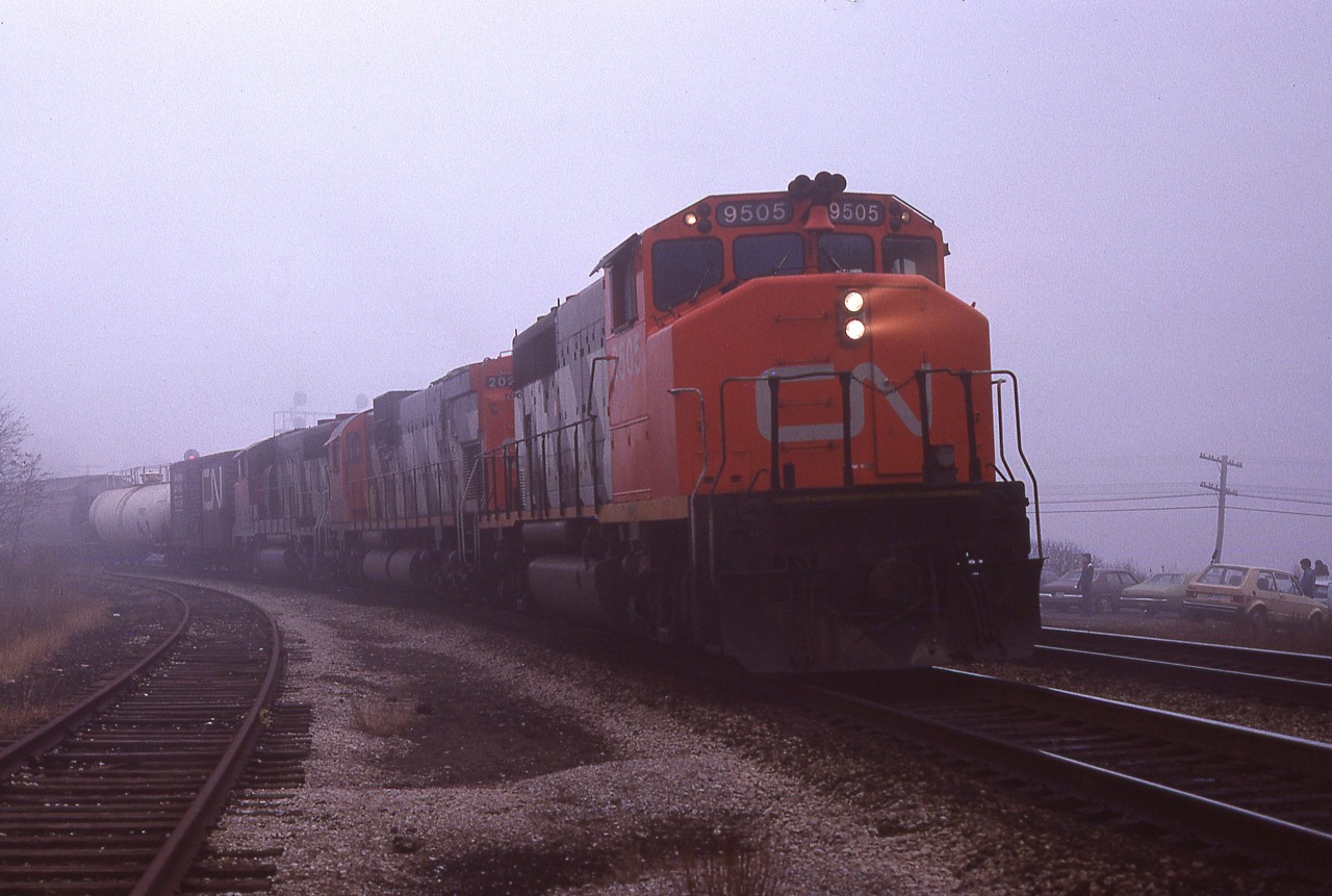 For whatever reason I did not get to recording the unit numbers behind this westbound freight led by CN 9505. It looks to be one heck of a gloomy day. Maybe my pen would not write. I dunno.  But note even with weather conditions about as lousy as they could get, outside of pouring rain; the usual gang is showing up as seen by the cars visible on the right.  Somehow, we made it all fun.  Cheers!!!