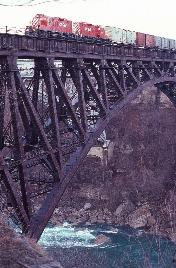 Since I never had the opportunity to be on a train over this bridge, I can only imagine what it would feel like looking out the window. Not like being on a road where you can see the shoulders. Gads!!  What a long way down.
This image is of CP 8227 and 8234, a pair of GP9u locomotives now gone from the system; on their way into Canada. When rail traffic left downtown Niagara Falls in 2000, the bridge was abandoned. Too costly to tear it down.