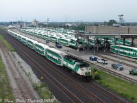 GO Transit F59PH 559 is pushing hard on the tail end of Lakeshore West train #921 as it flies by GO's Willowbrook Yard maintenance facilities in Mimico, as viewed from the Islington Avenue overpass. A few new MP40's have infiltrated the ranks of seasoned F59's under the canopy awaiting dispatch for PM rush hours. Visible are units 561, 610, 544, 531, 608, and 601. F59 562 can be seen in distance, turned west(!) to serve as the Willowbrook shop switcher. A few more new MP40's were also scattered on the property at the time.<br><br>Compare this "classic GO green" shot to a more present-day view (one for the Time Machine files) taken by Terry O'Shell of Willowbrook Yard in 2026, with more than a few more shades of Metrolinx green visible: <a href=https://www.railpictures.ca/?attachment_id=58939><b>https://www.railpictures.ca/?attachment_id=58939</b></a>. A few other changes noted since then have been the demolition of the old National Silicates plant in the background, and the redevelopment of the Mimico Correctional Centre visible by the "Jailhouse Lead" in the distance (it was interesting walking by the very tall chain-link fence topped with barbed wire around the border, keeping the inmates inside the grounds).<br><br>Today's trip wasn't for GO units however, rather, to shoot the lineup of brand new EMD Class 66 units from the GMD London plant that were stored at CN's Mimico Yard to the south, awaiting forwarding by CN to the Toronto Port Authority for shipment overseas:<br><a href=http://www.railpictures.ca/?attachment_id=16369><b>http://www.railpictures.ca/?attachment_id=16369</b></a><br><a href=http://www.railpictures.ca/?attachment_id=5167><b>http://www.railpictures.ca/?attachment_id=5167</b></a><br>