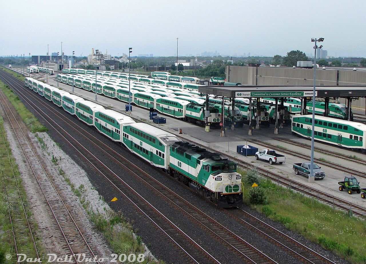 GO Transit F59PH 559 is pushing hard on the tail end of Lakeshore West train #921 as it flies by GO's Willowbrook Yard maintenance facilities in Mimico, as viewed from the Islington Avenue overpass. A few new MP40's have infiltrated the ranks of seasoned F59's under the canopy awaiting dispatch for PM rush hours. Visible are units 561, 610, 544, 531, 608, and 601. F59 562 can be seen in distance, turned west(!) to serve as the Willowbrook shop switcher. A few more new MP40's were also scattered on the property at the time.

Compare this "classic GO green" shot to a more present-day view (one for the Time Machine files) taken by Terry O'Shell of Willowbrook Yard in 2026, with more than a few more shades of Metrolinx green visible: https://www.railpictures.ca/?attachment_id=58939.

Today's trip wasn't for GO units however, rather, to shoot the lineup of brand new EMD Class 66 units from the GMD London plant that were stored at CN's Mimico Yard to the south, awaiting forwarding by CN to the Toronto Port Authority for shipment overseas:
http://www.railpictures.ca/?attachment_id=16369
http://www.railpictures.ca/?attachment_id=5167
