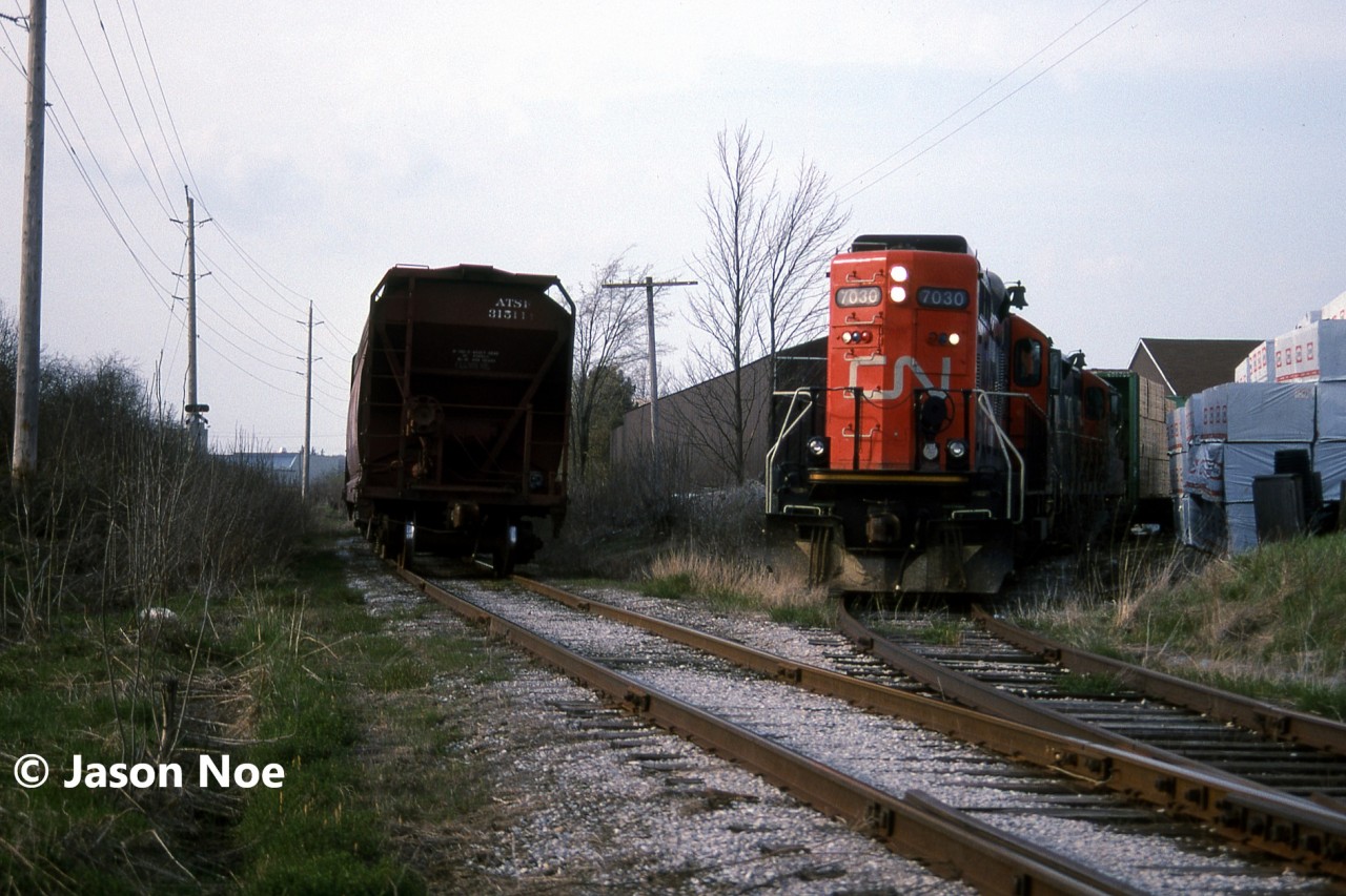 The CN 15:30 Kitchener Job is viewed setting-off one loaded lumber car at Fairway Lumber in St. Jacobs on the Waterloo Spur with 7030 and 4141. The job was on their return trip south to Kitchener when they stopped to set-off the car. At the time, the job only operated with two units when it was necessary and on this day, both Nutrite and Sulco Chemicals in Elmira had received several cars. The springtime was always a busy period for Nutrite receiving hoppers.