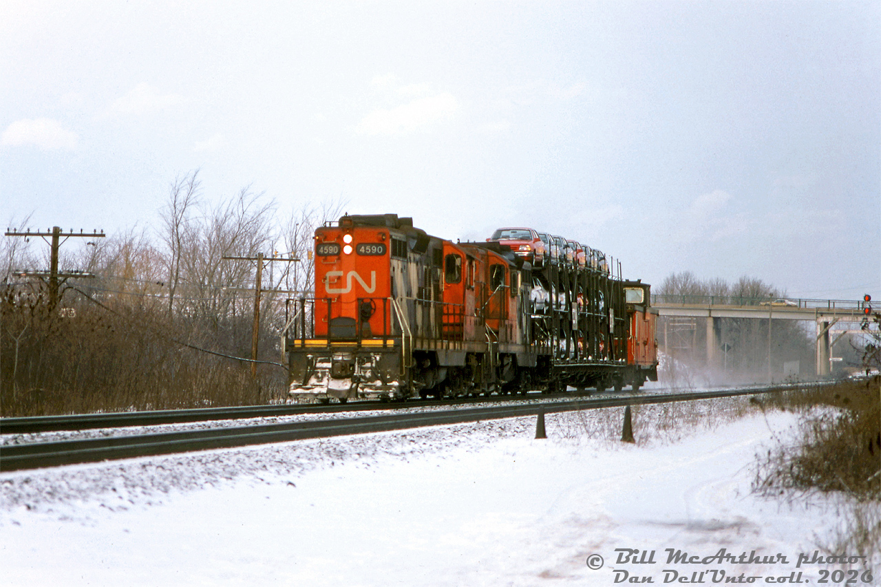 CN GP9's 4590 and 4563 hustle westbound through Aldershot by Lemonville Road, with what must have been a single "hot rack" load in tow full of brand new Ford Tempos and Mercury Topazes from the Ford plant in Oakville. At the time CN's GP9RM rebuilt program was underway, and trailing unit 4563 would soon be rebuilt into GP9RM 7227 later that year. 4590 would become 7065 in 1992.Bill McArthur photo, Dan Dell'Unto collection slide.