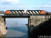 CN GP40-2LW 9616 and GP38-2W 5571 handle train #547 eastbound on the Oakville Sub above the Desjardin Canal in Hamilton.<br><br>This photo, as well as being a nice view of the canal, provides a good study between the more powerful 3000 horsepower turbocharged GP40-2LW model, and the less powerful non-turbo 2000 horsepower GP38-2W model: note the difference in fans (3 vs 2), radiator sizes (larger vs shorter), and exhaust stacks (single for turbo vs a pair for non-turbo plus a paper air filter box).<br><br>This view also shows the difference in overall height between the taller, lighter "L" frame CN ordered on most of its early widecab GP40-2LW units (taller frame members caused the unit to ride higher), versus the normal frame on the GP38-2W model. This was apparently to allow the GP40's to maintain the correct overall weight, with the added weight of a Canadian Safety Cab and larger 3000 gallon fuel tanks for road service, versus the standard frame GP38-2W (and later GP40-2W) units ordered with a smaller 2300 gallon fuel tank.<br><br><i>Reg Button photo, Dan Dell'Unto collection slide.</i>