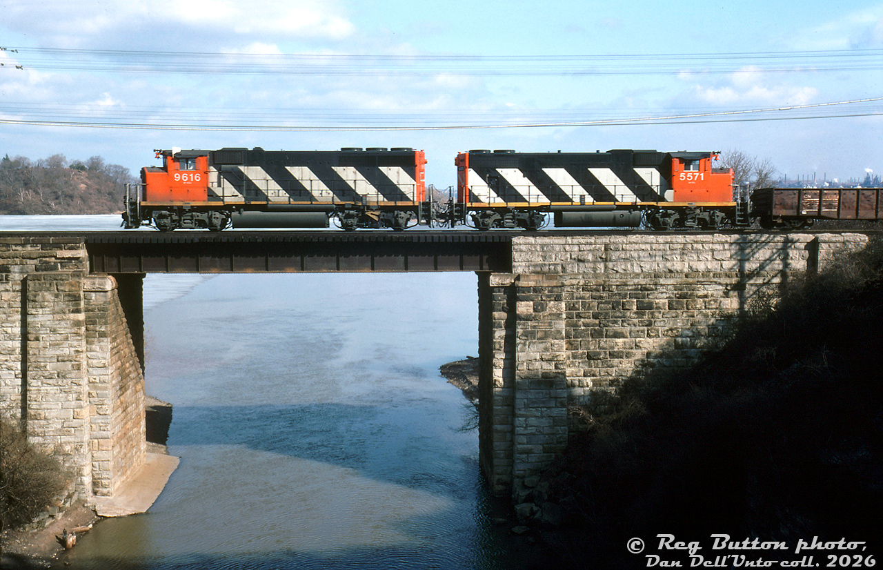 CN GP40-2LW 9616 and GP38-2W 5571 handle train #547 eastbound on the Oakville Sub above the Desjardin Canal in Hamilton.

This photo, as well as being a nice view of the canal, provides a good study between the more powerful 3000 horsepower turbocharged GP40-2LW model, and the less powerful non-turbo 2000 horsepower GP38-2W model: note the difference in fans (3 vs 2), radiator sizes (larger vs shorter), and exhaust stacks (single for turbo vs a pair for non-turbo plus a paper air filter box).

This view also shows the difference in overall height between the taller, lighter "L" frame CN ordered on most of its early widecab GP40-2LW units (taller frame members caused the unit to ride higher), versus the normal frame on the GP38-2W model. This was apparently to allow the GP40's to maintain the correct overall weight, with the added weight of a Canadian Safety Cab and larger 3000 gallon fuel tanks for road service, versus the standard frame GP38-2W (and later GP40-2W) units ordered with a smaller 2300 gallon fuel tank.

Reg Button photo, Dan Dell'Unto collection slide.