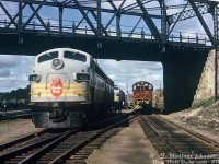 Power for both Montreal and Toronto sections of Canadian Pacific's eastbound Canadian sits waiting under the bridge at Paris Street, as CP S2 7091 shuffles passenger cars east of the station in Sudbury. CP FP9 1406 and an F7B sit ahead, while CP FP7 1423, an F7B and FPA2 sit on the other side of the bridge by the fuel racks.<br><br>During CP operation, eastbound train <a href=http://www.railpictures.ca/?attachment_id=6502><b>#2 "The Canadian"</b></a> from Vancouver split at <a href=http://www.railpictures.ca/?attachment_id=52322><b>Sudbury</b></a>, with one train heading east to <a href=http://www.railpictures.ca/?attachment_id=8230><b>Montreal as train #2</b></a>, and the other south to Toronto as <a href=http://www.railpictures.ca/?attachment_id=49537><b>train #12</b></a>. The reverse happened with westbound trains <a href=http://www.railpictures.ca/?attachment_id=31854><b>#11 from Toronto</b></a> and <a href=http://www.railpictures.ca/?attachment_id=4120><b>#1 from Montreal</b></a> combining at Sudbury into <a href=http://www.railpictures.ca/?attachment_id=41882><b>#1 for Vancouver</b></a>. Extra passenger cars would be kept at Sudbury, added or removed from consists as they were broken up or combined. Switching power was typically one of the locally-assigned <a href=http://www.railpictures.ca/?attachment_id=41125><b>7000-series</b></a> MLW S2 units.<br><br><i>J. Wollatt photo, Dan Dell'Unto collection print.</i>