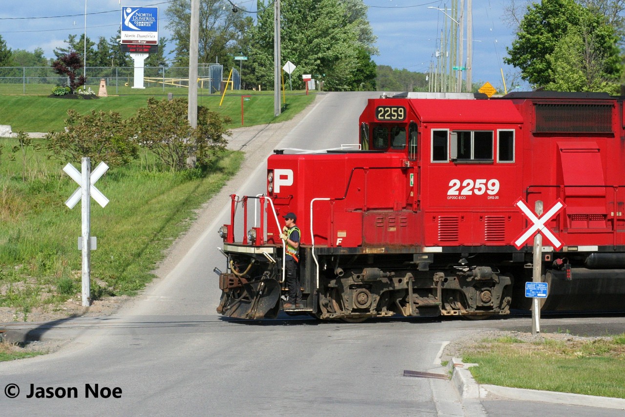 An extra CPKC Wolverton Job with GP38-2 3040 and GP20C-ECO's 2307 and 2259 is viewed about to cross Greenfield Road in Ayr, Ontario on the Ayr Pit Spur. The crew was returning to Wolverton after setting-off auto racks on the Waterloo Subdivision for the Toyota Plant in Cambridge. However, they had a lengthy stop at Ayr to switch the busy FS Partners facility on the spur.