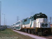 Heading eastbound into the city after dipping under the <a href=http://www.railpictures.ca/?attachment_id=36009><b>Queen Elizabeth Way</b></a> overpass, GO Transit GP40TC 500 speeds through the Swansea area of Toronto with a 7 bilevel Lakeshore West train bound for Union Station. One can see the water tower for the <a href=https://www.railpictures.ca/?attachment_id=47105><b>Mr. Christie Lakeshore Bakery</b></a> in the background, and part of the Oshawa Group warehouse (next to the Ontario Food Terminal) on the right. The signals for the <a href=http://www.railpictures.ca/?attachment_id=43270><b>Mimico East</b></a> interlocking are visible in the distance.
<br><br>
<i>Original photographer unknown, Dan Dell'Unto collection slide.</i>