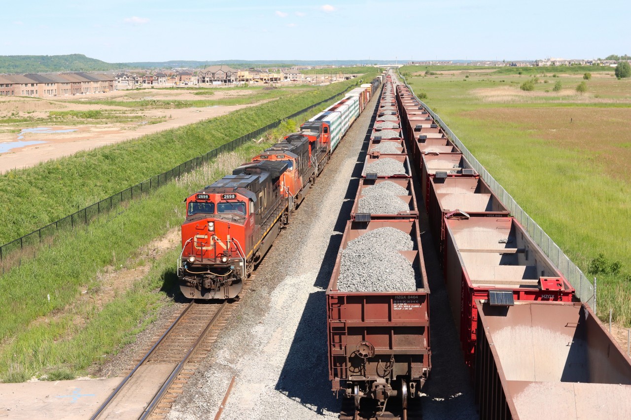 A425 IC 2698 CN 5670 CN xxxx (578 axles) slides by Work Train CN xxxx CN xxxx with Herzog Ballast Cars tied down on the Construction Tracks (future North and South Tracks) between Derry Mile 36.9 and Ash M 38.8. The Work Train crew is walking alongside the empty cars on the future South Track to get to the power and prepare for the days work dumping ballast on the future North Track. Part of the ongoing track capacity improvements to support the future Milton Logistics Hub.