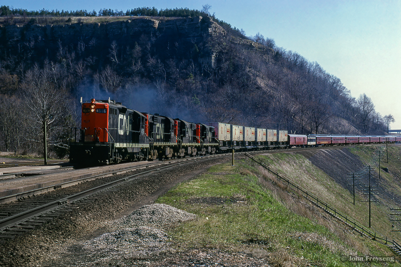 Touring the nation as part of the 1967 centennial celebrations, one of the two trains carrying the Canadian Armed Forces Military Tattoo climbs the grade at Dundas, bound for an evening performance in Sarnia.  

The tattoo was designed to operate as three parts, with part 1 being the initial tours of the two trains from late March through mid May, performing arena shows with 450 performers.  One consist was made up of CN equipment, known as 'train A,' and carried the 'blue' group of performers, while the other was made up of CP equipment, aka 'train B,' carrying the 'red' group of performers.  In late May, both groups combined, and additional performers added, bringing the total to about 1700 for the next stage of shows; stadium performances from late May through August.  The final part of the tattoo would be smaller shows beginning in late summer, and wrapping up in mid October.  Further reading can be found on Keith Allan Wilson's Tattoo 1967 website, as well as the itinerary of events for the year.

Look waaaay up on the cliff, just in front of the prominent tree at top centre.  Two figures can barely be seen taking in the action right on the peak; Jim Brown, and Tom Henry.  More photos to come, and more details on this  can be found in Tom Henry's article in the April 1967 UCRS newsletter.

Scan and editing by Jacob Patterson.