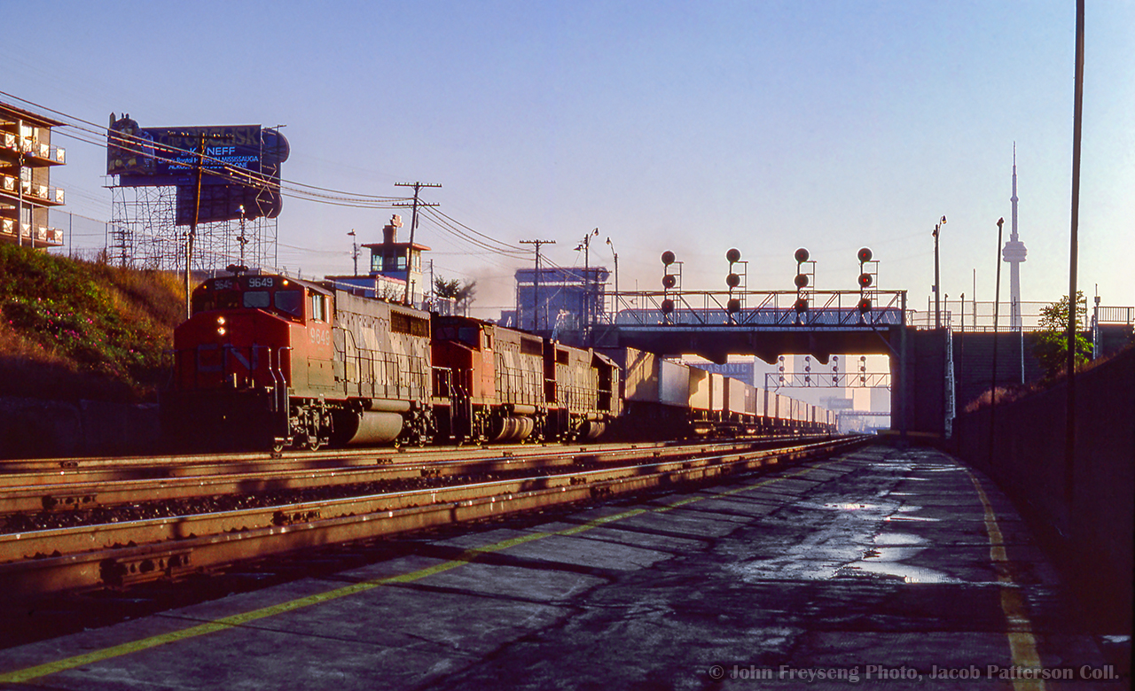 Westbound out of Toronto, a TOFC train rolls beneath Dufferin Street, passing the old Exhibition station, out of service about eleven years now.  This station was opened in 1912 to serve the annual Canadian National Exhibition at the nearby Exhibition grounds, replacing an earlier station nearby. It continued to see use until 1968, when the new Exhibition GO station was opened east of Dufferin Street, on the site of the original Exhibition station. These platforms would see one more bit of service for the 1979 CNE due to crowding at Exhibition GO, with this location being temporarily named "Dufferin Gates." Since then, the old platforms have remained abandoned and overgrown, with stairs to Dufferin Street fenced off.


John Freyseng Photo, Jacob Patterson Collection Slide.