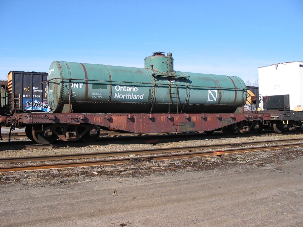 Kit bashed  
Here's one for the modelers. 
ONT 1699 (ex-ONT 100201-100299 series flat car, NSC built June 1940) has ex-ONT 1595 'water storage only' tank strapped to its deck as they sit on a deadline in ONR's North Bay, ON yard May 4, 2004. 
Although it is now 24 years ago, I remember that day quite well as there was so much to view and shoot as I walked around the shops and yard for hours on that clear and sunny day. :-)