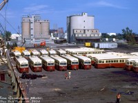 Due to the opening of the TTC's new Bloor-Danforth subway line in February 1966, and its subsequent extensions in May 1968, a chunk of the Toronto Transit Commission's fleet of PCC streetcars became redundant and were sold off. Alexandria, Egypt was the largest buyer, acquiring groups of TTC PCC's in both 1966 and 1968. The cars sold were the earliest TTC "air-electric" PCC cars (4000-4200 series, A1-A5 classes built new) and the oldest secondhand air-electric cars (4575-series, A10-class ex-Cincinnati), while newer cars stayed on the roster and continued in TTC service. <br><br>This photo taken by Tom Gascoigne pretty much sums things up nicely: down at the Toronto Port Authority, rows and rows of early TTC PCC air-electric streetcars sit at Pier 24, awaiting loading into the Mare Tranquillo for shipment to Egypt. They had been previously loaded onto flatbed trucks by the TTC at Russell Carhouse, and trucked down to the portlands for their final seafaring trip overseas. Some had already been loaded in the days prior, but many still sat on their trucks on the bare pavement awaiting the cranes parked nearby to hoist them onboard. In addition to the ship and port crews shown (evidently shirts were optional), some transit photographers and other spectators were aboard the ship and on the ground on this day to watch and document the loading process. Most were loaded by the mobile cranes off the pier, but a few streetcars were loaded onto a barge, floated to the other side of the ship, and loaded via barge crane aboard the other side.<br><br>According to sources, there were about 76 ex-TTC PCC cars being shipped out in this batch. As they were loaded aboard, they were crammed on every inch of available space including on top of the ships' holds, inside the ship's holds (apparently on top of a load of corn) and along the deck sides (all 76 apparently made it on a single trip). Cars lined up below in the first row are former TTC 4202, 4278, 4579, 4169, 4580 and 4221. Second row: 4576, 4188, 4587, 4575, 4279, 4251. Known car on far right in front: 4111. Across the upper back on the right: 4217(?), 4229, 4577, 4231. Cars loaded aboard included 4235, 4200, 4022, 4258, 4205 and many more. "Barge cars" included 4270, 4178 and 4232. Lined up along the portside edge (out of sight to the right) were 4581, 4268, 4213, 4242, 4225, 4250, 4223, 4043, 4006, 4293 & 4007, awaiting loading once this batch were finished. Other early cars that had not been resold were mostly sold for scrap and cut up, but the first PCC car, 4000, did manage to escape both fates and is now preserved at the Halton County Radial Railway.<br><br>In Egypt, many of the ex-TTC streetcars were pressed into service, with some modified to operate in multiple car trains of 2-car sets and later 3-car sets. The final ones were apparently retired in the mid-1980's.<br><br>For the industrial rail enthusiasts and old Toronto history buffs, this view in the portlands was shot off the starboard side of the Mare facing east towards Cherry Street, with Polson Street to the south running along the right. Pier 24 here did not have rail sidings, but Pier 35 to the north did (including a large dockside crane). Industries visible include the two Canada Cement silos (served by rail, note the CN "slab-side" covered hoppers), Texaco Canada (tank farm on the other side of Cherry Street, also served by rail, note "Sky Chief Gasoline" advertisement) and part of the old Hearne generating station visible beyond. On the right was the Continental Can Co. (note ONR boxcar spotted on the siding along Polson St., the building today is home to a variety of businesses including Rebel nightclub). Beyond that to the south (on the far right in the distance) was an auto recycling yard known as Industrial Metals Ltd (that part of <a href=https://www.youtube.com/watch?v=z_eCasv1-MY><b>an episode of Police Surgeon</b></a> was filmed at). All were accessed by rail off the Q400 Ashbridges Bay switching lead that ran next to Cherry Street.<br><br><i>Tom J. Gascoigne photo, Dan Dell'Unto collection slide.</i>
