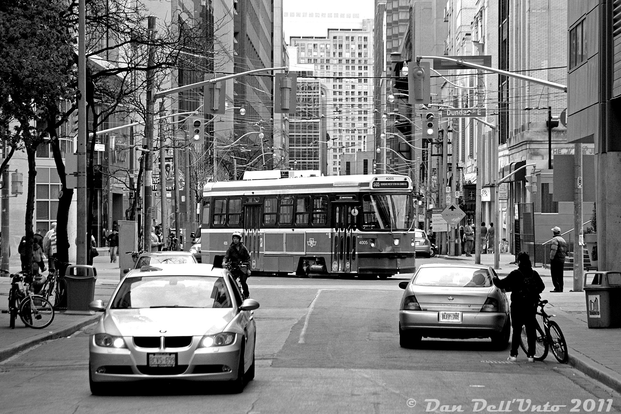 A busy street scene unfolds on the door of Ryerson University's campus: cars, pedestrians and cyclists go about their business as TTC CLRV 4005 (one of the original six prototypes built by SIG) turns westbound off Victoria Street back onto Dundas after a 505 route diversion or short turn. By this time, part of Victoria and Gould had been closed off to create a walkable campus area for students, with access remaining here for the old Ryerson parking garage that 10 Dundas East was built around.