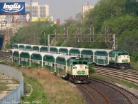 Little Train, Big Train: a pair of GO Transit F59PH units handle two morning rush hour trains leaving the Union Station Rail Corridor onto the CN Oakville Sub near Strachan Avenue: GO 550 off Bradford (Barrie) line train #802 pauses with its short equipment move waiting for the light off the bypass/"High Line" tracks to proceed west to Willowbrook Yard, passed by in-service 547 buzzing by at speed on the tail-end of full-sized Lakeshore West train #477.<br><br>The ever-present Inglis sign offers its morning insights of "Nothing can be changed until you start(?) to find the issue", that smokestack belongs to one of the old restored buildings in Liberty Village, and I believe those apartment buildings are off Dufferin Street.<br><br>At the time, GO's smallest consists were "L6" trains (locomotive and 6 bilevels), the smallest possible to keep the required 2500-series "5A" accessible car as the 5th car in order to line up correctly with the accessibility platforms. Some Georgetown, Bradford and other lines used them on less-patronized trips, while the standard "L10" consist (locomotive and 10 bilevels) was the maximum-sized train GO would run to do the heavy lifting on busier trips. At the time GO was all-F59 all the time, and their HEP abilities limited trains to a maximum of 10 cars (most station platforms were also only that long).