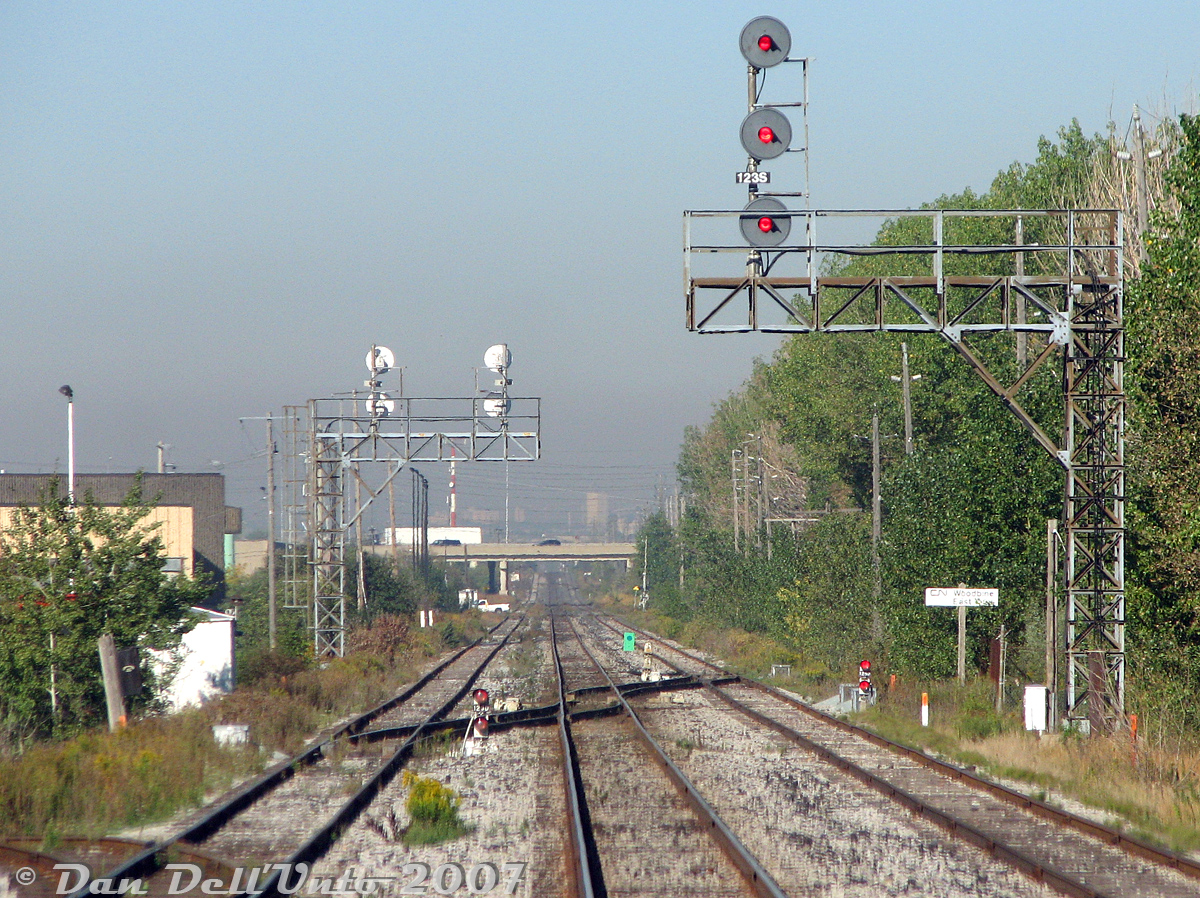 I had a request from someone for some more corridor photos, so here's a neat one: we are, yet again, riding the rear end of GO Transit cab car 237 on train #252 (Bramalea-Union), having just jolted through the crossover switches at CN Woodbine East, Mile 12.3 CN Weston Sub, through the dip between Malton GO station in the far distance (by Woodbine West) and Etobicoke North GO station (by the former CN Rexdale). We're on the mainline track, with the north and south service tracks on either side. On the left, you can see one of those old classic wooden CN phone boxes mounted on a pole, probably a relic from the 60's or 70's.

This was a good, quick stretch with one single grade crossing at Carlingview Drive (note pickup truck in distance and grade crossing gates) leading to Entrance Road that looped around Woodbine Racetrack (out of frame to right). That row of tall trees along Entrance Road by the tracks was a nice place for people to pull off and park under during the day. Passing by, I often wondered what all the individuals in their cars were doing there, possibly taking an afternoon nap, enjoying lunch, or engaging in other activities that involved discreetness and a quiet place (like enjoying a good book, of course).

There were a few spurs and sidings to nearby customers in the Attwell/Disco Road area, that once included IPEX (pipe), Canron's old Toronto eastern structural plant (involved in CN Tower construction, originally Disher Steel Co. hence "DISCO" Road), Westeel Rosco, some paper companies, but not including the Gazzola Brothers asphalt plant on the left. There were also a pair of runarounds/sidings just past Carlingview near Highway 427 to handle the local traffic, that would also see wing gondolas from the nearby McDonnell-Douglas/Boeing Malton plant sometimes. Refer to this nice 1971 aerial and this 1991 aerial for some industrial goodness.

Since the purchase of the Weston Sub by GO/Metrolinx in 2009, this stretch has since been upgraded with 4 mainline tracks, the interlocking plant rebuilt to the west for the Pearson Spur and renamed Wice, all the local sidings and runaround removed, and Carlingview Drive grade-separated. This exact spot near Highway 27 will be home to the new Woodbine GO Station in the future.
