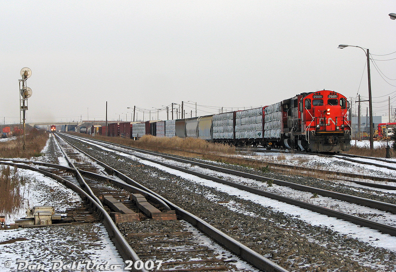 It was a cold November Saturday but there were trains to be had: CN #577, the regular CN MacMillan Yard to CP West Toronto transfer run for interchange traffic, is busy working Malport Yard with a nice combo of GP9RM 7001 and GP40-2LW 9418. On the north track of the Halton Sub, three rebuilt SD40 units (CN 6020, 6016 & WC 6944) are working hard moving #399 past Airport Road overpass and bearing down on the crossing at CN Torbram, giving us just enough time before the bells and lights go off to cross over to the other side for a wider shot. The hum of the nearby switch heaters, offering no warmth to us, were keeping the switch for the western Brampton Intermodal Terminal lead at Torbram warm (note the small storage yard along the lead, off to the left). This was all a side-trip while waiting out the yard set with the GMD-1 inside BIT to get back to work around the Highway 7 overpass.CN Torbram was at one point a great spot to shoot from and easily accessible from the Torbram Road grade crossing (name likely from TORonto Gore + BRAMalea), until CN turned it into an underpass during 2015-2019. Malport Yard (MALton + airPORT) was once an all-freight yard (at the time local job #578 was based out of it, that switched some of the Bramalea area industries, and I believe a #579 that switched the Weston Sub at night, with #577 dropping and lifting traffic for Mac), but in recent years was closed down, most of the tracks removed, and rebuilt to handle overflow intermodal traffic from BIT (with improved security measures to keep photographers away).