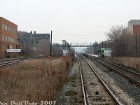 This gloomy November shot gives a much nicer view than a Spring one where all the vegetation is grown in and blocking everything: GO Transit's old iteration of their Bloor GO station, seen from the back of GO cab car 201 on morning train #252 (Georgetown line, Bramalea-Union) as it clickity-clacks down the jointed stick-rail CN Weston Sub after making its station stop to detrain a lone passenger or two. This whole area was a bit of a sleepy place rail-wise in the afternoons, as aside from the <a href=http://www.railpictures.ca/?attachment_id=59215><b>odd VIA</b></a> and afternoon <a href=http://www.railpictures.ca/?attachment_id=32906><b>Union-Bramalea GO trains</b></a>, no freight ran on either line (all the action was in the distance by the signals around the CN-CP <a href=http://www.railpictures.ca/?attachment_id=7128><b>West Toronto diamond</b></a>). The neat element here is CP's "West Toronto" mileboard sign for the Galt Sub that runs parallel on the left, although at the time it was mostly just <a href=http://www.railpictures.ca/?attachment_id=682><b>Milton-line GO trains</b></a> using it (the Strachan to West Toronto section may have already been purchased by GO some years prior).<br><br>The orange building on the left is <a href=https://www.railpictures.ca/?attachment_id=59668><b>The Crossways Mall</b></a> complex, then still a relic of the 70's inside (raw brick décor, large round glass light fixtures and earth tone tiles). Behind that is the old Ideal Aluminum building off Dundas Street West, and the Wallace Avenue pedestrian bridge spanning the rail corridor from Dundas to Ernest Avenue. Some other office or apartment complex is on the right off Perth. The picturesque G. Solway & Sons scrapyard is hidden behind it but was still a going concern near the station (hard to miss the giant piles of scrap metal from the GO train every day). There was yet no West Toronto Railpath on the right, at the time CP's former TG&B line (the <a href=http://www.railpictures.ca/?attachment_id=38483><b>"Bruce Service Track"</b></a>, aka the S-Yard Lead) had long been abandoned and removed, as were the dual CN-CP interchange tracks just north of the station (although ties remained in the ground).<br><br>The <a href=http://www.railpictures.ca/?attachment_id=6752><b>amenities were sparse</b></a> at Bloor GO Station: both brick-enclosed open entrances to the platforms were accessed off stairways roughed into the Bloor Street West railway underpass wall, between the bridge spans. The east side platforms were the most used (lots of people did the short jog along Bloor from nearby <a href=http://www.railpictures.ca/?attachment_id=18073><b>Dundas West Subway Station</b></a> and boarded westbounds home here) so it got the corrugated square station shack that was perennially never open, and multiple shelters. The west side platforms were sparse except for a pair of shelters (and a payphone!). One wonders why they never added an extra platform here for the Milton-line trains. Substantial station upgrades have since been made here for improved GO and UPX service, and a direct TTC subway-GO train connection is finally happening.
