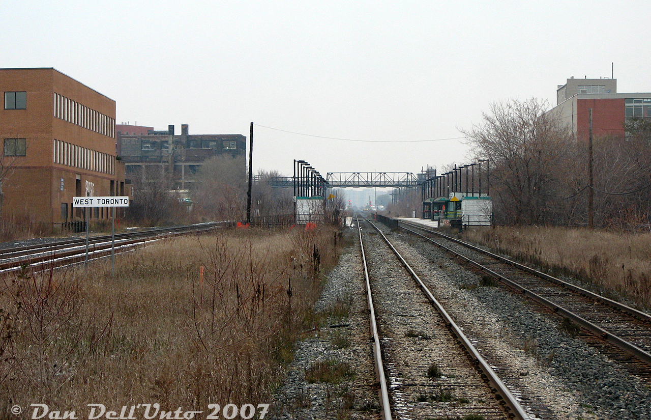This gloomy November shot gives a much nicer view than a Spring one where all the vegetation is grown in and blocking everything: GO Transit's old iteration of their Bloor GO station, seen from the back of GO cab car 201 on morning train #252 (Georgetown line, Bramalea-Union) as it clickity-clacks down the jointed stick-rail CN Weston Sub after making its station stop to detrain a lone passenger or two. This whole area was a bit of a sleepy place rail-wise in the afternoons, as aside from the odd VIA and afternoon Union-Bramalea GO trains, no freight ran on either line (all the action was in the distance by the signals around the CN-CP West Toronto diamond). The neat element here is CP's "West Toronto" mileboard sign for the Galt Sub that runs parallel on the left, although at the time it was mostly just Milton-line GO trains using it (the Strachan to West Toronto section may have already been purchased by GO some years prior).

The orange building on the left is The Crossways Mall complex, then still a relic of the 70's inside (raw brick décor, large round glass light fixtures and earth tone tiles). Behind that is the old Ideal Aluminum building off Dundas Street West, and the Wallace Avenue pedestrian bridge spanning the rail corridor from Dundas to Ernest Avenue. Some other office or apartment complex is on the left off Perth. The picturesque G. Solway & Sons scrapyard is hidden behind it but was still a going concern near the station (hard to miss the giant piles of scrap metal from the GO train every day). There was yet no West Toronto Railpath on the right, at the time CP's former TG&B line (the "Bruce Service Track", aka the S-Yard Lead) had long been abandoned and removed, as were the dual CN-CP interchange tracks just north of the station (although ties remained in the ground).

The amenities were sparse at Bloor GO Station: both brick-enclosed open entrances to the platforms were accessed off stairways roughed into the Bloor Street West railway underpass wall, between the bridge spans. The east side platforms were the most used (lots of people did the short jog along Bloor from nearby Dundas Subway Station and boarded westbounds home here) so it got the corrugated square station shack that was perennially never open, and multiple shelters. The west side platforms were sparse except for a pair of shelters (and a payphone!). Substantial station upgrades have since been made here for improved GO and UPX service, and a direct TTC subway-GO train connection is finally happening.