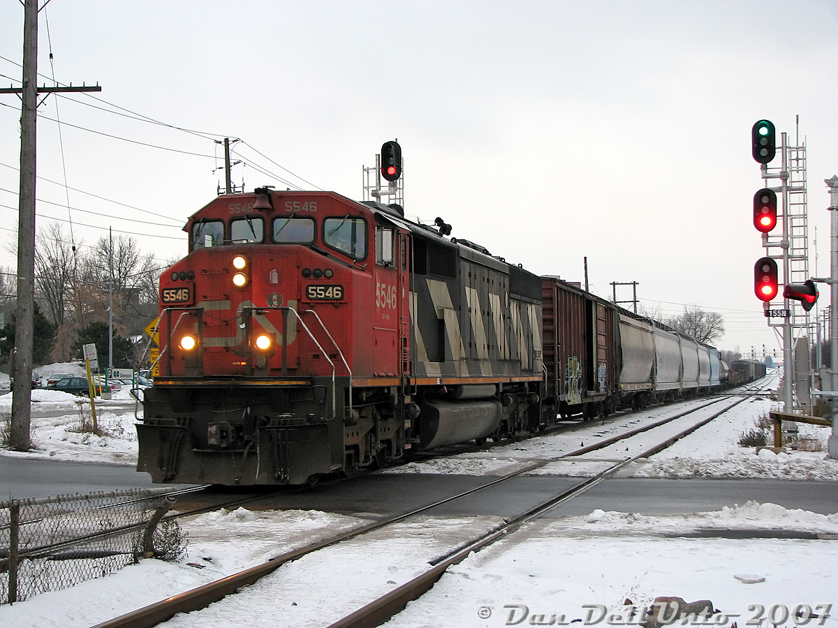 CN's Draper Taper cowl units looked sort of weird leading freight trains solo, almost as if there should be some Budd or LRC passenger cars trailing behind instead of freight cars. CN SD60F 5546 on a "One-Unit Wonder" leads a short eastbound freight (possibly #330) into downtown Brampton, its head-end just crossing Mill Street as the rest of the train thumps the Brampton diamond. Compared to an earlier photo, note the new signals here and in the distance (installed during the summer), and the old CN-CP interchange track switch now removed.