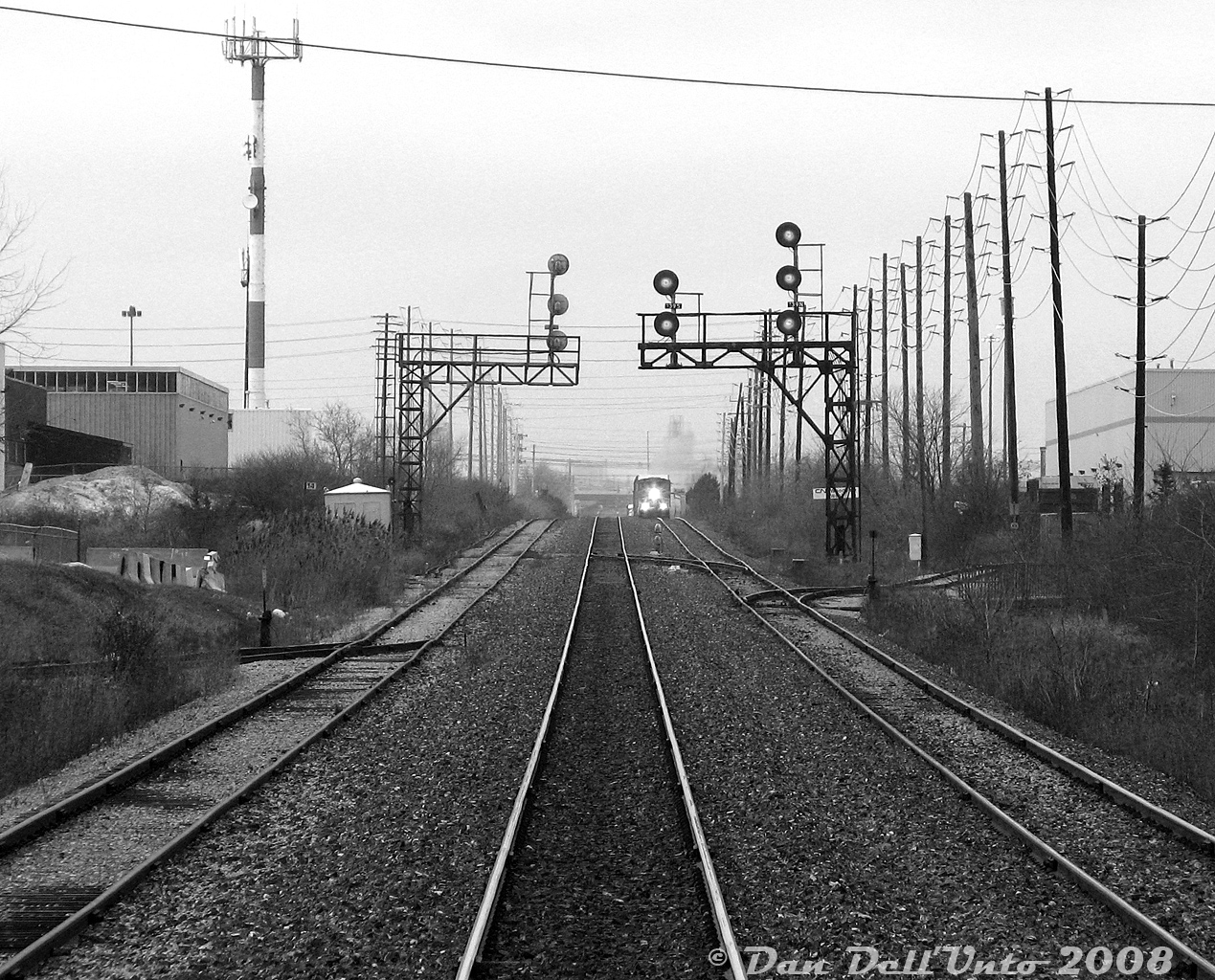 Here's a complementary view to go with Woodbine East along the Weston Sub: CN Woodbine West, Mile 14.1 CN Weston Sub. Our view is trailing eastbound aboard GO cab car 241 on train #260 (Bramalea-Georgetown) after making our stop at Malton GO station, hidden by the approaching train. CN #577 with sister GP40-2LW units 9411-9410 is about to crest the grade on the north service track and will follow us downhill, enroute to West Toronto to interchange traffic with CP. In the distance one can see the Highway 407 overpass at Halwest, and faintly the Owens Illinois glass plant in Brampton.The siding on the right is for the Home Depot's Malton lumber distribution facility (receiving boxcars and centre beam flatcars). The switch to the left was the old American Can Lead that lead into the Northwest Dr industrial area, serving customers in the business park that once included IGA, American Can and Kuehne & Nagel (Brenntag Canada was the last active customer before removal). Fairmont Motor Company even had a warehouse and siding at 6320 Northwest Dr. This area of Malton also used to be home to a variety of aircraft manufacturing facilties, including the large McDonnell-Douglas/Boeing Malton plant at Airport & Derry (of Avro Arrow fame), Orenda Engines, and DeHavilland (now the International Centre), all of which used to receive rail service from various sidings off the Weston Sub.The tracks here have since been upgraded, and the signal bridges replaced. Most of the old sidings and spurs have been pulled up, with the only remaining customer being Home Depot.