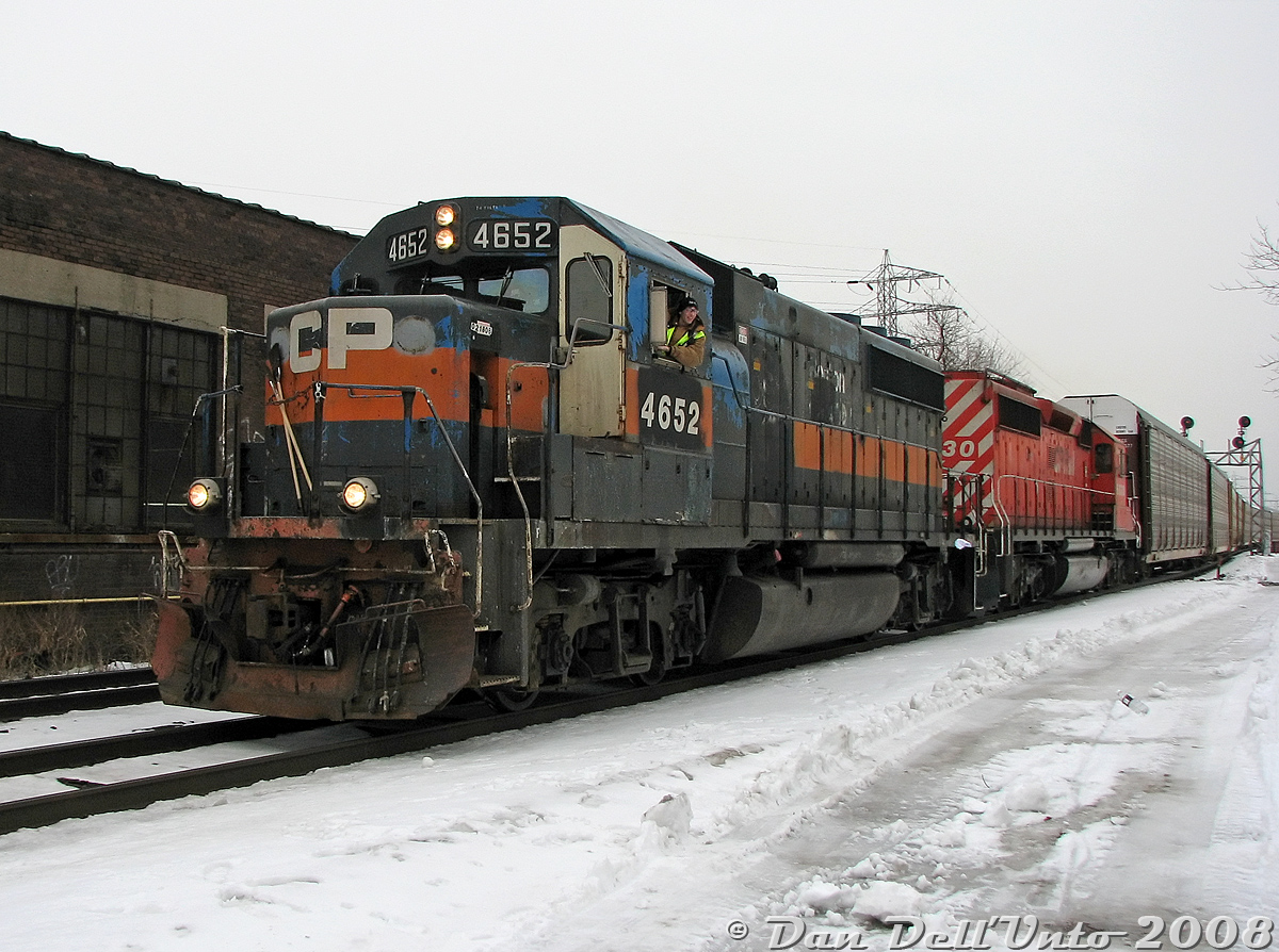 Rough unit in a rough hood. You never know who or what might show up down by the train tracks in some parts of Toronto, in this case a ratty and well-worn CP GP40-2 4652 rolls through Bartlett Avenue crossing on the North Toronto Sub with SD40-2 6030, working train #T56, the transfer from Toronto (Agincourt) Yard to West Toronto/Lambton Yards. The conductor on this day, known in some circles as "oeuf", is wearing his signature Pink Floyd touque as he leans out of his trusty steed, having just generously contributed/chucked a document-wrapped water bottle to the bystanders and miscreants trackside. He later expressed great preference and fondness for this "greasy" set of power, despite its outward rat-rod appearance.When CP purchased these eight former Guilford GP40-2 units from Helm Leasing (4650-4657), they weren't too quick to repaint them, and some got fresh red paint while others continued to run in patched fading Guilford grey/orange for years, some so long that the original B&M blue started showing through. Apparently as the story goes, the guys down on the former D&H got so sick of seeing the Guilford paint on these units (bad memories from the D&H's Guilford era?) that they roller-brushed 4650 and 4653 red themselves and applied non-standard lettering. 4652 wasn't so fortunate, and the unit continued to run around the Toronto and Ontario area eluding the paint shop as the unofficial "Guilford heritage unit" (even causing a large wreck on the Belleville Sub in 2009) until it was finally sidelined and retired (since sold to Northern Plains RR, maybe they'll paint it someday).