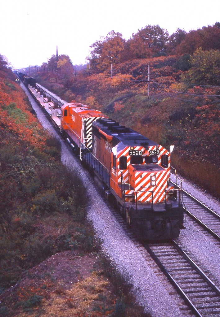 Crisp fall day along the CN Oakville sub near a location now known as 'Snake'. CP 5528 leads an unknown MLW in the image shot from what I refer to as the 'Cemetery Bridge', just east of the Bayview's Laking Gardens where all the fans hang out.
Don't know for sure, so I just assume this  train is the 'Starlite" heading for Hamilton's Aberdeen yard.
Note the old brick company chimney in the background. And a relic of the past, that triangular 'Junction 1 mile' sign on the left. Back in those days there were a number of them around, but now, all gone. Not even in anyone's collections that I know of.