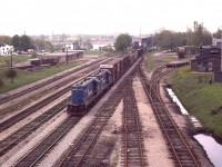 To clarify the location of the old CN Crew Hostel which I offered up the other day, here is a view of the eastern most part of CN Fort Erie trackage, taken 10 years before the Hostel closed.  It can be seen on the right; and the old MCRR/TH&B station on the left, with a Conrail transfer behind CR 5439 and 5441 just coming into Canada.  The USA is seen in the far background. Lots to look at here. In the background also, on the right, a yellowish rail car is parked on a stub. This was a Boeing car; one was spotted here on occasion due to the Fleet Aircraft company located nearby.
It is a rather gloomy day, and although this is not a factor, I scribbled in my notes that Mount St. Helens had blown up the previous day.  Just a historical note.