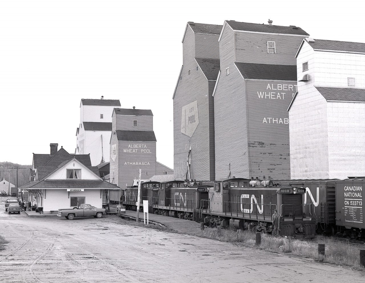 At the very north end of CN’s Athabasca subdivision (originally Canadian Northern’s subsidiary Edmonton & Slave Lake) was the town of Athabasca, on the south side of the Athabasca River.  A turn from Edmonton on Sunday 1980-09-21 with branchline GMD1s CN 1008 + 1007 +1009 brought empties for loading at the several grain elevators, and as seen here, collected a train of loads to take back southward.  That depot was then occupied by the Athabasca District Senior Citizens Society, and survives to this day administered by the Athabasca Heritage Society.
