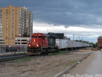 An excellent leader: CN RoadRailer #145 rolls through downtown Brampton under threatening evening skies, past the VIA/GO station, with CN SD40u 6013 in charge of tonight's long train of Triple Crown trailers originating at MacMillan Yard. 6013 was originally built as SD40 5059 in 1968, and rebuilt to Dash-3 standards by AMF Technotransport in 1995 (one of 29 units upgraded, <a href=https://cptdb.ca/wiki/index.php/Canadian_National_Railway_6000-6028><b>6000-6028</b></a>).<br><br>This clear wide-open shot wasn't possible before (and isn't now) as most of the foreground was previously overgrown with heavy brush, bordered by a chain link fence. It was all bulldozed clear for construction of a second (south) Brampton Station platform on this side of the tracks. Half of Railroad Street, that we're standing on, had also been closed off to traffic for the work. Today, new platform shelters and brush block this shot once more.