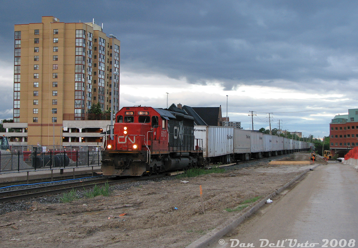 An excellent leader: CN RoadRailer #145 rolls through downtown Brampton in the evening, past the VIA/GO station, with CN SD40u 6013 in charge of tonight's long train of Triple Crown trailers originating at MacMillan Yard. 6013 was originally built as SD40 5059 in 1968, and rebuilt to Dash-3 standards by AMF Technotransport in 1995 (one of 29 units upgraded, 6000-6028).
This clear wide-open shot wasn't possible before (and isn't now) as most of the foreground was previously overgrown with heavy brush, bordered by a chain link fence. It was all bulldozed clear for construction of a second (south) Brampton Station platform on this side of the tracks. Half of Railroad Street, that we're standing on, had also been closed off to traffic for the work. Today, new platform shelters and brush block this shot once more.