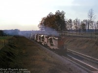 Leaving a trail of diesel exhaust in its wake, a CN freight rolls into London with GP9 4566 leads a mixed-bag lashup of an SD40, GP9, GP40, RS18 and GP40-2LW, heading eastbound through Hyde Park on the Strathroy Sub.
<br><br>
<i>Gord Taylor photo, Dan Dell'Unto collection slide.</i>