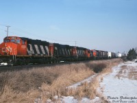 This CN #381 has a nice mixed-bag lashup of CN power consisting of GP40-2LW 9554, C630M 2033, GP40-2LW 9419, SW1200RM 7314 and GP9RM 7028. It's seen heading west through CN Norval on the Halton Sub, at Mississauga Road grade crossing on the western outskirts of the City of Brampton.<br><br>The silos in the distance marked a farm that used to exist just north of the present-day Mount Pleasant GO Station (demolished in the mid-2000's). The Norval Farm Supply on the right lasted into the early 2010's before the property was cleared for more Brampton development, and the grade crossing here was replaced with a grade-separation overpass in the mid-2020's.<br><br><i>Peter Jobe photo, Dan Dell'Unto collection slide.</i>