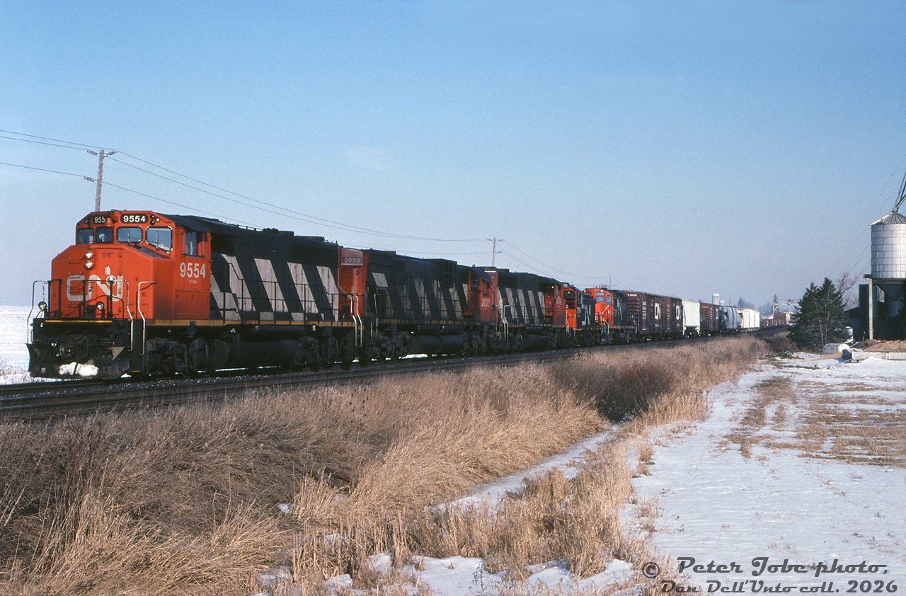 This CN #381 has a nice mixed-bag lashup of CN power consisting of GP40-2LW 9554, C630M 2033, GP40-2LW 9419, SW1200RM 7314 and GP9RM 7028. It's seen heading west through CN Norval on the Halton Sub, at Mississauga Road grade crossing on the western outskirts of the City of Brampton.

The silos in the distance marked a farm that used to exist just north of the present-day Mount Pleasant GO Station (demolished in the mid-2000's). The Norval Farm Supply on the right lasted into the early 2010's before the property was cleared for more Brampton development, and the grade crossing here was replaced with a grade-separation overpass in the mid-2020's.
Peter Jobe photo, Dan Dell'Unto collection slide.