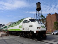 6/02/21 GO MP54AC #668 is shoving hard on its consists as it heads up the Newmarket Sub towards Barrie, Ont. The locomotive is just passing Wallace Ave, in The Junction area of Toronto. The big water tower in the background has an interesting history.

Canadian General Electric (CGE) Ward Street Works plant in Toronto's Junction-Wallace Emerson neighbourhood, which is famous for its towering wooden water tower. 

The factory, built in the early 1920s at 224 Wallace Avenue, once manufactured lamp bases and electrical supplies. It has since been transformed into vibrant creative, studio, and commercial spaces. The old plant even served as the former home of video game developer Ubisoft. 

The CGE complex is best known for a few distinct, prominent local landmarks:
* The Wooden Water Tower: It is one of the very last original wooden water towers still standing in the city. The City of Toronto gave it heritage status in 1993.

* The Ghost Sign: Painted high atop the water tower is a faded, historic sign that reads, "Canadian General Electric Company Limited - Ward Street Works." 

This photo will never be seen again due to the Metrolinx expansion of the Newmarket Sub. If you visit today, they have installed a second track. Sarting at Bloor St the double track rises up to a grade that eliminated the very busy CP/CN diamond at West Toronto. The times, they are a changin
