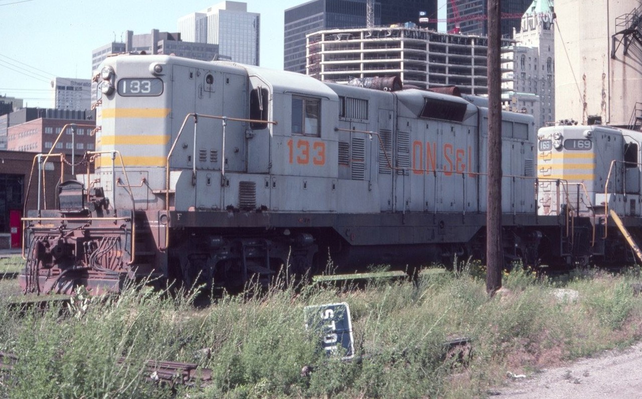 Quebec, North Shore and Labrador GP9 # 133 is seen near Toronto Union Station in July of 1982. The fabulous Royal York Hotel is seen peeking through in the background. All this area is of course changed today.