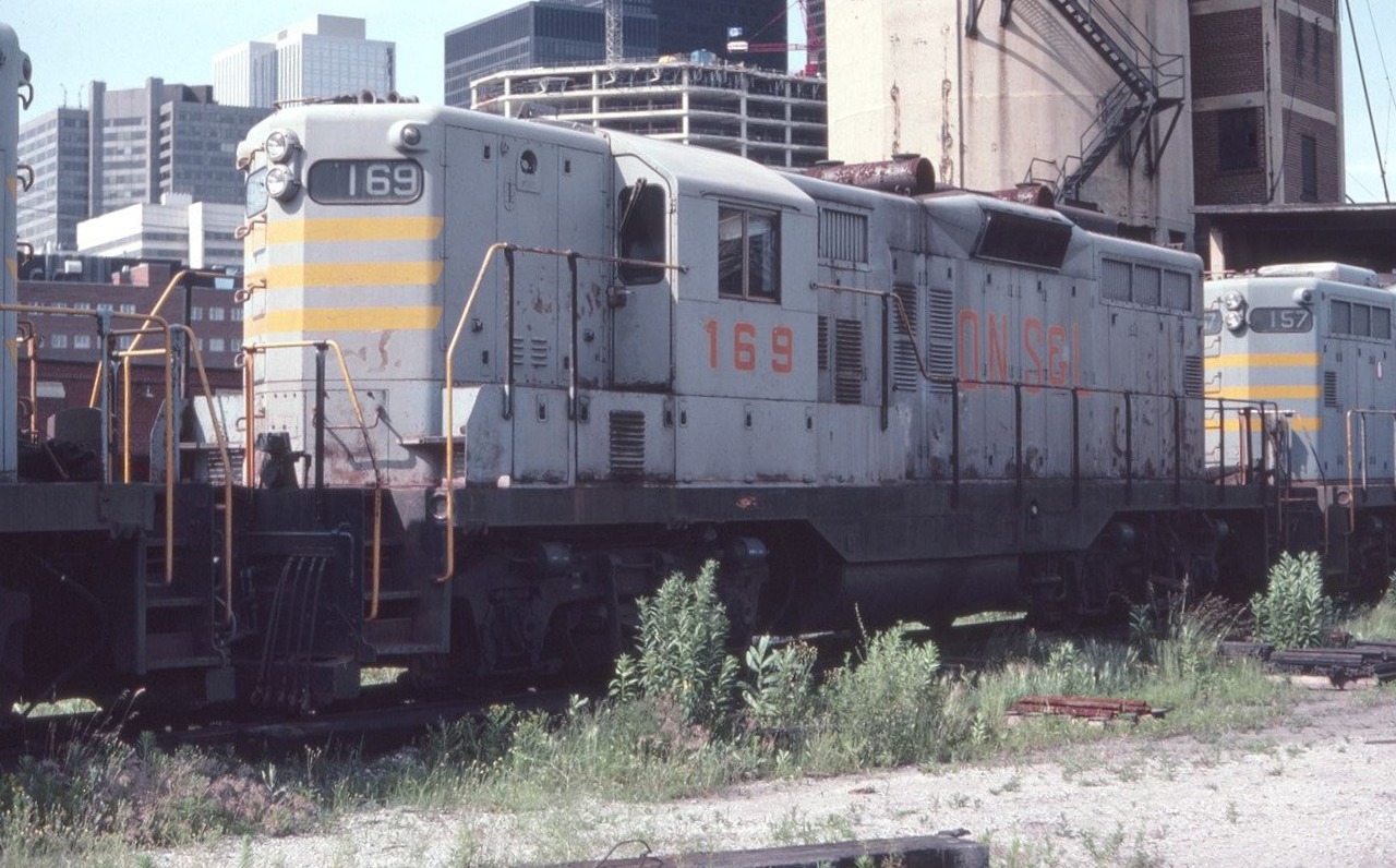 Quebec North Shore and Labrador GP9 #169 is seen near Toronto Union Station in July of 1982. There is an interesting mix of old railroad structures and city skyline in the background. All changed today.