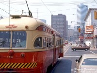 A somewhat unconventional streetcar photo: TTC PCC 4457 on Dundas Street East waits at the light westbound at Jarvis Street, doors open for any last-minute passengers. More than a few open windows with elbows poking out suggests it's a warm day, with other riders at the back going about reading their papers. The elevated left-hand vantage point might be from aboard one of those British double decker buses the TTC tried in tourist service around this time, sitting behind in traffic. Another PCC car approaches in the distance from around <a href=https://www.railpictures.ca/?attachment_id=56452><b>Church Street</b></a>, and beyond that the towering Eaton Centre shopping mall and office tower at <a href=http://www.railpictures.ca/?attachment_id=39305><b>Yonge Street</b></a>. The brown building in the middle is the Bond Place Hotel.<br><br>But the real attraction here (in a matter of speaking) is the Warwick Hotel, another one of those seedy establishments of ill-repute in the general Yonge-Dundas area of Toronto. "Star Strip Revue", "Stripperrama", and "Nude Girls" advertise the kind of entertainment one may expect to witness inside, as well as rooms charging a $7 per person rate, rather than per hour. Other photos show retail shops sharing space on the ground level of the hotel included Lisa Variety at the corner, and some place called the "Nut Nest" (a nut shop, selling nuts). Aptly named.<br><br>Research shows the Warwick Hotel was originally built as a hotel known as the Royal Cecil Apartments, owned by James Franceschini, an Italian immigrant who originally came to Canada from the old country before the war with no money and no English, but who picked up a pickaxe and went on to found and grow the Dufferin Construction empire. The Royal Cecil was originally just a hotel, and featured dance bands during the 1940/50's, but changed to its later questionable offerings by the 60's. City of Toronto Archives photos show the wrecking ball would come knocking on the Warwick in a few years, brought to the ground by Teperman Wrecking during 1980-81. The site would become home to a rather uneventful parking lot for many years to follow.<br><br><i>Roger Jenkins photo, Dan Dell'Unto collection slide.</i>