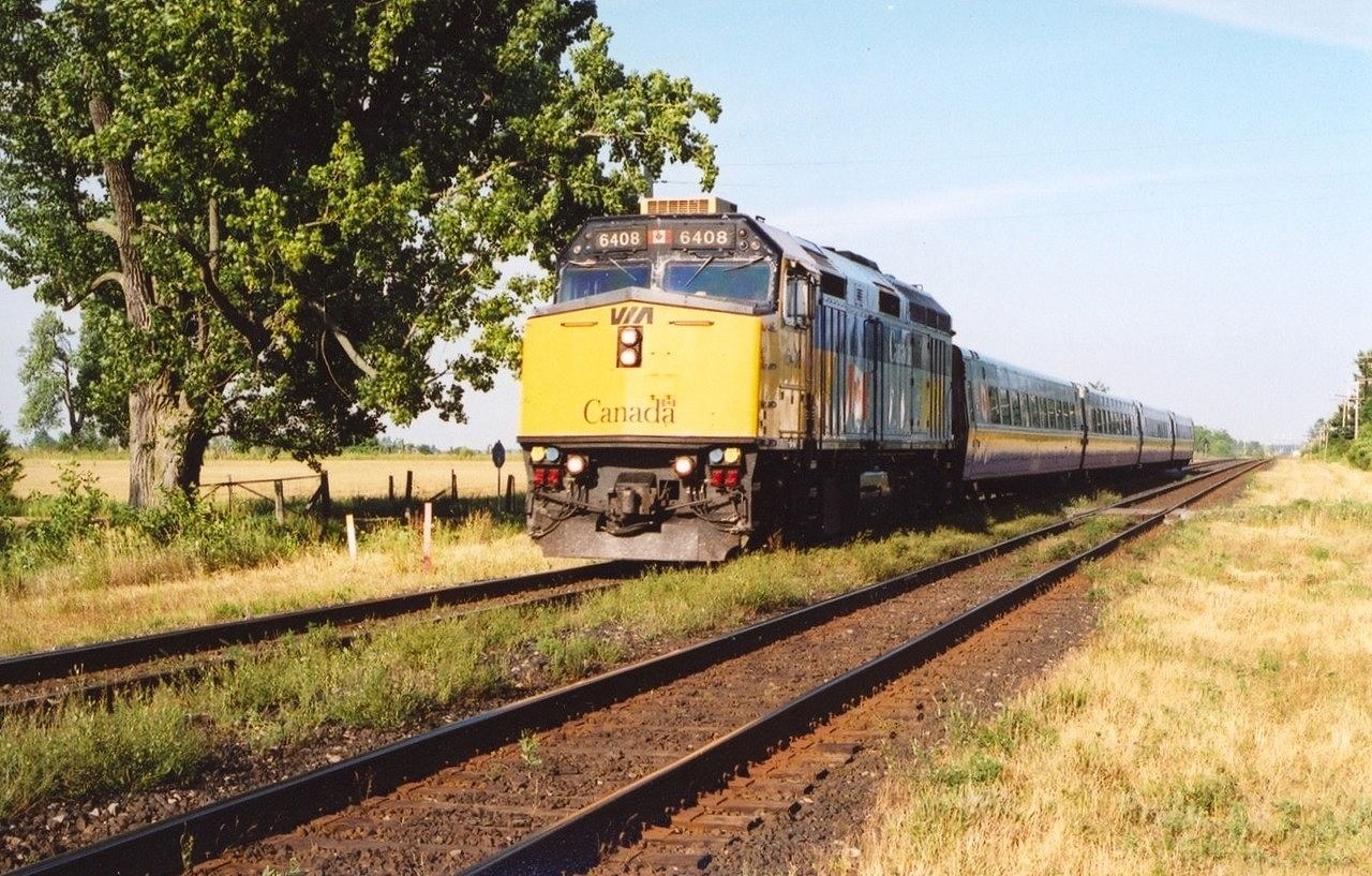 Via GMD F40PH 6408 leads a westbound past the station in Gananoque, Ontario, in July of 2004. This unit later was given a Spiderman livery. A recent (2023) Google Maps view shows that the big old tree on the north (left) side of the tracks is not looking so great.
