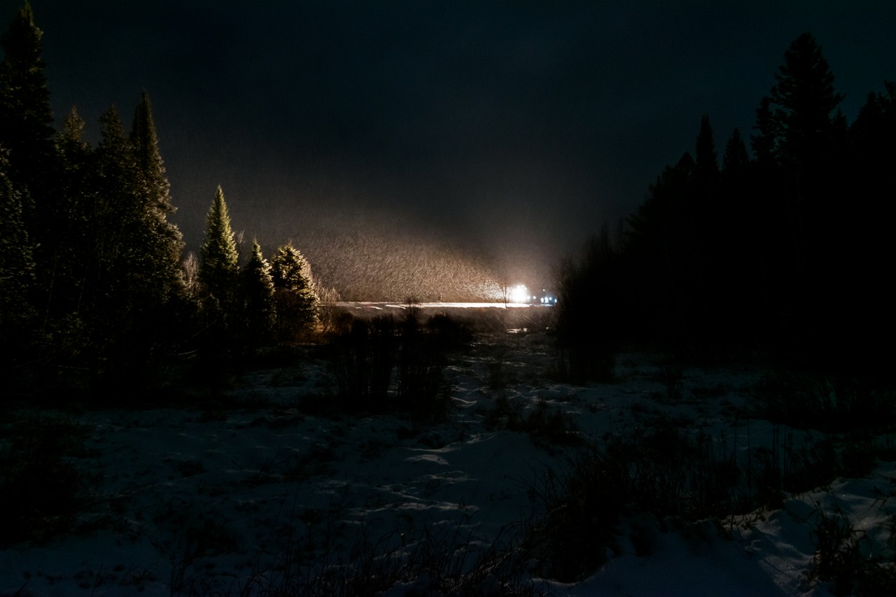 The realities of northern railroading. A freight train had brake issues amid this snowstorm, and when its crew ran out of hours it caused a cascade of impacts. Via's Canadian #1, already behind schedule, got stuck behind it on the CPKC Parry Sound Sub and its crew also died. To make matters worse, the Holiday Train was also caught behind #1, and many people gave up waiting on its final stop of the night in Sudbury, choosing instead to escape homeward from the cold, blowing snow.
After shooting the Holiday Train at the French River I too was heading back home, but heard about the dispatch-nightmare unfolding. I got a rough sense of where #1 was stuck and braved an unplowed sideroad to find it. Soon after, a taxi pulled in with the relief crew. We chatted and walked together on a laneway toward the tracks, but I held back once I saw this clearing. The snow was just a bit too thick to pull off the exact shot I envisioned, but if you look closely near the centre of the frame, you'll see their ghostly frames walking toward the wall of light from the lead unit.
Checking my notes from that night, the Holiday Train was only pulling into Sudbury some 45 minutes after its scheduled showtime of 21:15. I was already home editing my photos by then! With yet another summer heatwave blasting Ontario, it's easier to appreciate these cold nights.