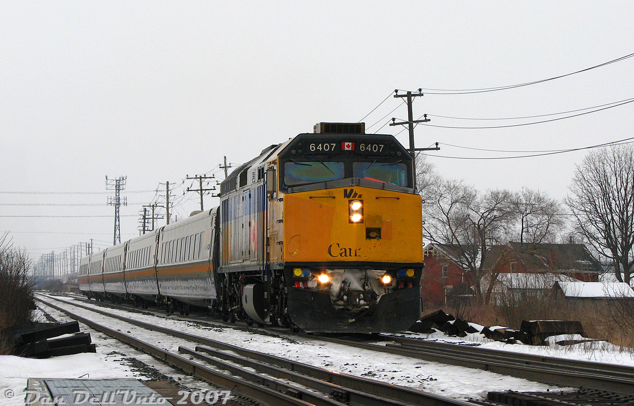 With some spare time in downtown Brampton on an overcast winter's afternoon, the first stop was our old favourite haunt: Fletcher's Creek bridge for VIA #84, seen bearing down on the bridge on time with its tail end just clear of the McLaughlin Rd. underpass on the final approach to its downtown Brampton station stop. By this point in time some of the VIA Rail F40PH-2D fleet had seen better days and were looking a bit shabby, including today's unit 6407. Sent from Guelph with love was this peach of a leader, showing off its large front nose dent, Grade 5-level paint patching, faded/missing front lettering, and of course the MU flap up (something about broken latch mechanisms, IIRC). It was rehabilitated a few years later and put on the straight and narrow when it emerged from the F40 rebuild program.

The old red brick farmhouse on the right was the "Fletcher House" (located right by Fletcher's Creek, naturally) built circa 1840. It and the Fletcher farm it stood on pre-dated the CN/Grand Trunk line here by a few decades, and had seen more than its fair share of steam and diesel engines pass by (see farm just NE of grade crossing at upper left here). At some point during Brampton suburbanization the old farm became a garden centre, and the old farmhouse at the back of the property was retained and continued to be lived in (possibly rented out). The garden centre wound down operations around 2021-22 and the property was put up for sale. The farmhouse received a heritage designation from the city in 2020, but experienced one of those mysterious overnight fires in 2022 and was deemed a total loss, making it conveniently (too conveniently?) a good spot for some townhouses or condos. So it goes for another piece of Brampton heritage, like many other old farmhouses in the recent past.

Next stop was Mount Pleasant for the afternoon VIA #85 (photo soon).